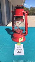 Front view of red vintage kerosene lantern showing glass chimney, metal wire protection, and handle.