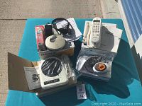 Assorted electronics items on blue table including Sony Walkman, Panasonic phone base, stereo cables, manuals, and other accessories