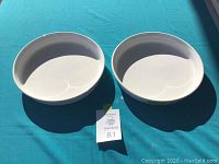 Two white ceramic pie plates on teal surface with shadows, showing front top-down view.