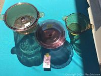 Set showing three pieces: two amber glass pots with lids and handles, and a purple glass baking dish.