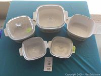 Overview of Corningware bakeware set showing five dishes including some with lids on blue tablecloth.