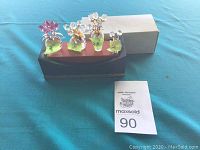 Overview of display stand with three crystal flower vases and one small crystal flower figurine on table with auction lot card