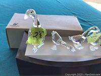 Lot showing four Swarovski crystal geese figurines and a matching display stand along with the Swarovski box on a blue cloth background.