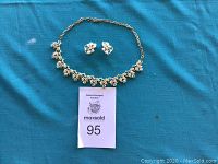 Full lot photo showing gold tone leaf motif necklace and matching earrings on blue fabric background.