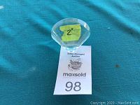 Top view of the clear crystal clam shell figurine with faceted edges and size marked as 2 inches on a piece of tape.