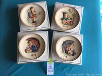 Four M.J. Hummel decorative plates displayed on a table showing the front imagery.
