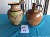 Photo showing both antique stoneware pieces, a cream and brown pitcher with embossed flower designs and a brown jug. Both placed on a blue surface with size labels on each.