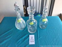 Three vintage crystal decanters with stoppers arranged on a blue cloth, each labeled with a number sticker.