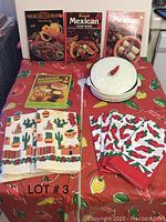 Full view of the lot items including 4 Mexican cookbooks, red printed circular tablecloth, white ceramic bowl with chili pepper lid, 2 hand towels with chili and cactus patterns, and 6 chili pepper napkins.