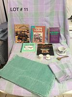 Lot includes four Oregon cookbooks, four placemats, one tablecloth with four matching napkins, ceramic bowl with wooden spoon, and two small shakers displayed on a purple and green plaid fabric background.
