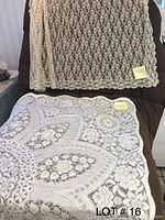 Two lace tablecloths draped over chair, showing intricate floral and geometric lace patterns with measurement stickers attached