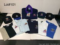 Photo of all apparel items including the navy blue jacket with purple collar, five shirts in various colors, and four black baseball caps, all with Grand Prix of Long Beach event logos embroidered.