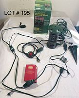 Photo shows an assembled green Yard-Line Outdoor Power Post with 9 outlets, coiled power cord with foot-activated switch, red transformer, grounding stakes, and original product box.