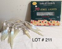 Photo of a string of icicle Christmas lights laid out in front of a box labeled '70 Jewel Lights' with colorful small bulb lights inside the box, image includes lot number 211.
