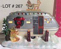 Front view of the silver ceramic roadside trailer Christmas decoration showing multicolored roof lights, wreath, Christmas tree, snowman, and NOEL candles on snowy base.