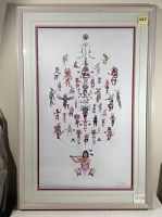 Photo shows framed print 'Kachina' by Marie Buchfink with a beige frame. The print depicts multiple colorful Kachina figures arranged in a symmetrical pattern, with a central seated Native American figure playing a flute. Dimensions noted as 23" x 35.25".