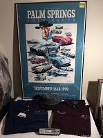 Framed 1990 Palm Springs Road Race poster tribute to Carroll Shelby with two dark colored race polo shirts, one navy blue large size and one burgundy extra large size, and a ballpoint pen in casing displayed in front.