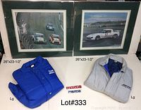 Photo showing two large framed signed Mazda prints with mattes, two Mazda jackets (blue and gray), one Mazda patch, and one Mazda name plate.