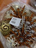 Assorted gold, silver, and amber Christmas ornaments including starburst finials and glittered balls in a plastic bag.