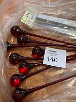 Lot of red hand blown glass ornaments with long narrow stems and spherical ends, packaged in plastic.