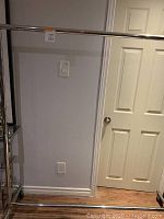 Full view of metal clothes rolling rack with horizontal hanging bar, vertical supports, and caster wheels, positioned against a wall and door in a room.
