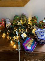 Photo of holiday string lights and several Christmas tree shaped and mailbox shaped decorative tins grouped on a wooden furniture surface