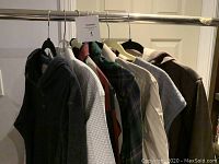 Seven men's tops hanging on a rail, showing various colors, patterns, and styles including hooded tops and dress shirts.