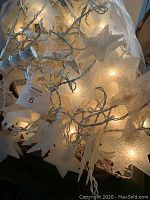 Multiple strings of white wired star-shaped Christmas lights with warm white glow, tangled together and tagged.