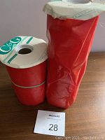 Front view of two tightly wrapped rolls of red brushed silk garland standing upright on a wooden surface, showing the brand label C&G on paper tops.