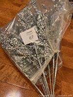 Bundle of shiny decorative stems with reflective beads wrapped in plastic on wooden floor.