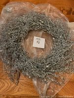 Full round sparkly Christmas wreath wrapped in plastic on wooden surface