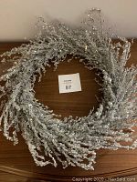 Full view of circular silver glitter Christmas wreath showing dense ornate branches.