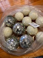 Photo of assorted silver sequin-covered and white textured spherical Christmas ornaments in a plastic bag.