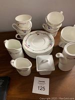 Photo showing stacked tea cups, saucers, creamer, milk jug, tea pot, and sugar dish arranged on wooden surface.