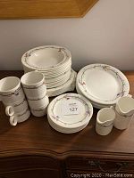 Full view of the china set showing stacked plates of varying sizes, coffee cups, milk jug and creamer with floral vine patterns on white china.