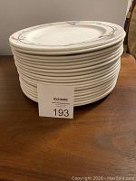 Stack of eighteen white dinner plates with floral pattern on rim stacked on wooden surface