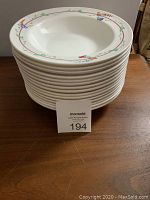 Stack of 15 white soup bowls with floral border, showing the top view of the bowls stacked evenly.