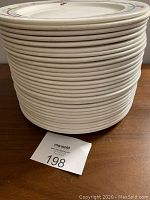 Stack of 28 white dinner plates on a wooden table, showing the thickness and quantity.