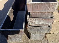 Four stacked and arranged dark gray metal rectangular planters showing weathered and worn surfaces with slight discoloration and patina from use.