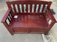 Cherry colour wooden hall bench with vertical slat backrest, armrests, and hinged seat providing storage space. Bench surface has visible scratches and wear.