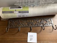 Photo showing a roll of white paintable textured wallpaper, 12 clear plastic shower curtain hooks, and decorative metal wall hook with five hooks.