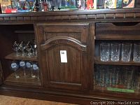 Glassware displayed inside wooden cabinet, showing various styles of cocktail glasses stored on shelves.