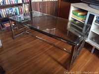 Full view of rectangular coffee table with glass top and chrome frame on wooden floor.