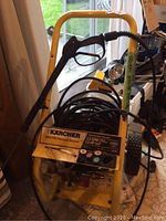 Front view of pressure washer showing yellow frame, coiled hose, and spray wand holder