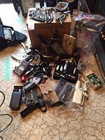 Photo showing a large mix of corkscrews, bottle openers, and bottle stoppers spread on the floor and a cardboard box.