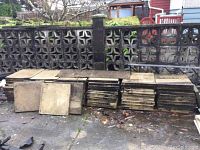The lot of 63 concrete paving stones stacked in multiple piles against a decorative concrete block fence outdoors on a paved surface.