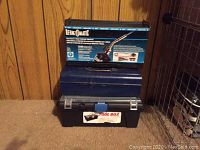 Photo of the Bernzomatic propane torch kit box on top of a blue toolbox with a black plastic toolbox underneath on a wooden floor with wood-paneled wall background.