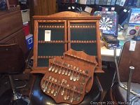 Two wooden framed display cases with glass doors and green felt interiors for holding souvenir spoons, and a wooden spoon rack with multiple souvenir spoons laid out.