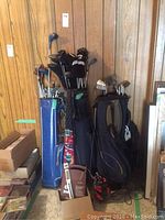Photo showing three bags filled with assorted men's and ladies' golf clubs including Power Built brand. Golf bags are blue, black, and red with various clubs.