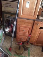 Photo showing metal barbell bar leaning against wooden cabinetry next to stacks of weight plates secured with red collars.